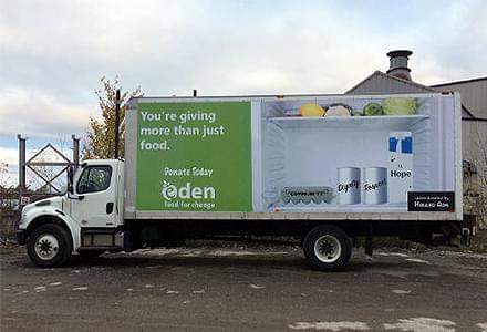 Truck advertising for Eden Food for Change on side of truck that is parked outside of factory.