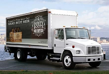 Mobile billboard advertisement for Iconic Brewing Co. on side of truck parked beside the lake