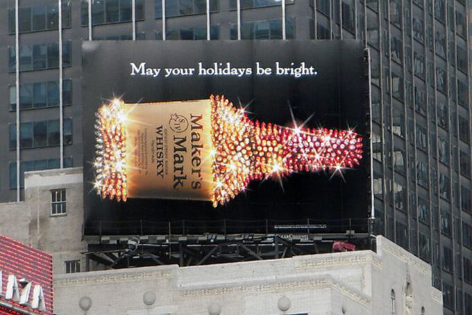An image of a large billboard on top of a building for Maker's Mark whisky. Has a bottle of whisky that's covered in rhinestones and glittering.