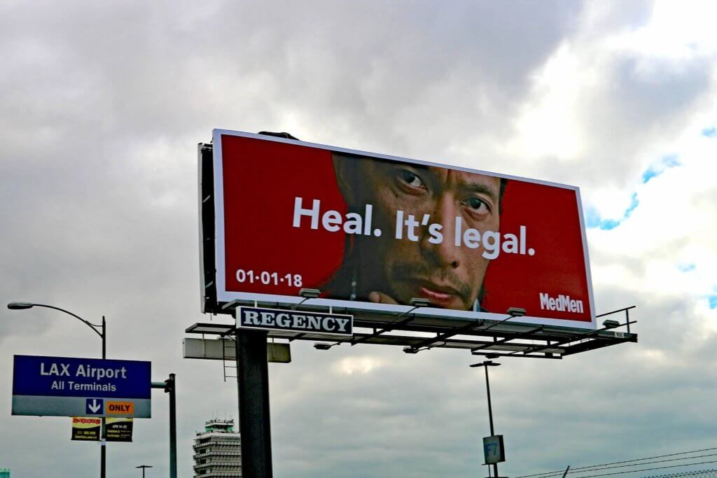 An image of a billboard for MedMen. Has a man looking serious with the text, "Heal. It's legal." overtop.
