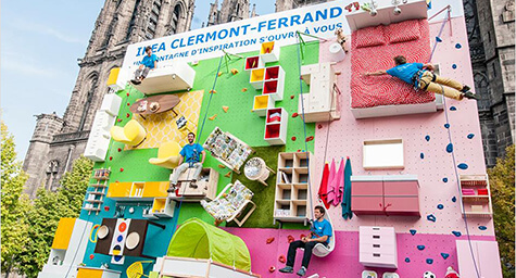 An image of an OOH ad. It's a rock climbing wall but the wall is decorated with IKEA furniture.
