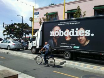 An image o fa truck-side ad that showcases the debut of a new tv show called "nobodies". There are three people on the billboard behind the title of the show.
