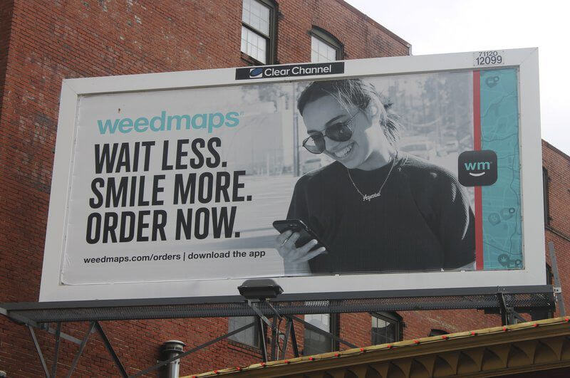 An image of a billboard ad for Weedmaps. Includes a girl smiling at her phone.