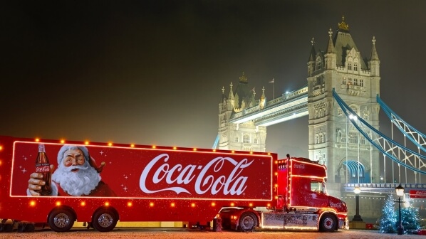 An image of a truck-side ad for Coca-Cola completely lit up with Santa on the side holding out a bottle of Coke.