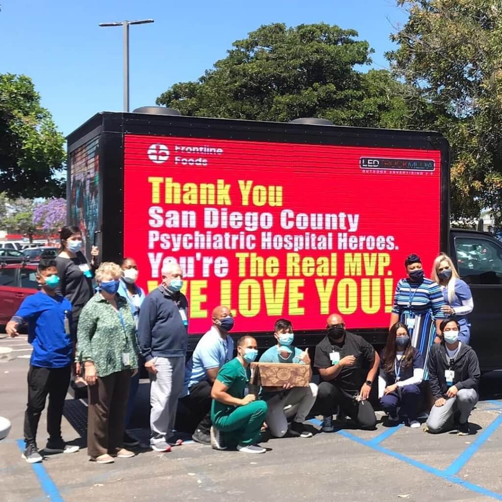 An image of a truck-side ad thanking healthcare professionals. A group of doctors and other health care workers all standing around the truck.