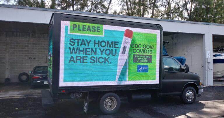 An image of a truck-side ad about staying home when sick to help slow the spread of COVID-19. 
