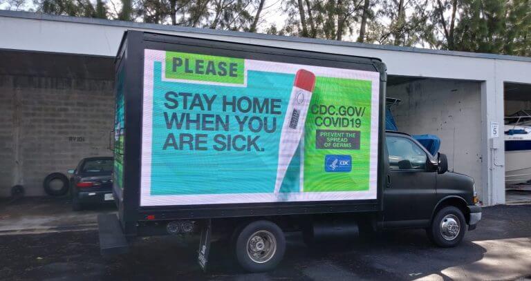 An image of a truck-side ad made by the CDC to inform people about COVID-19. Has the image of a thermometer on it.