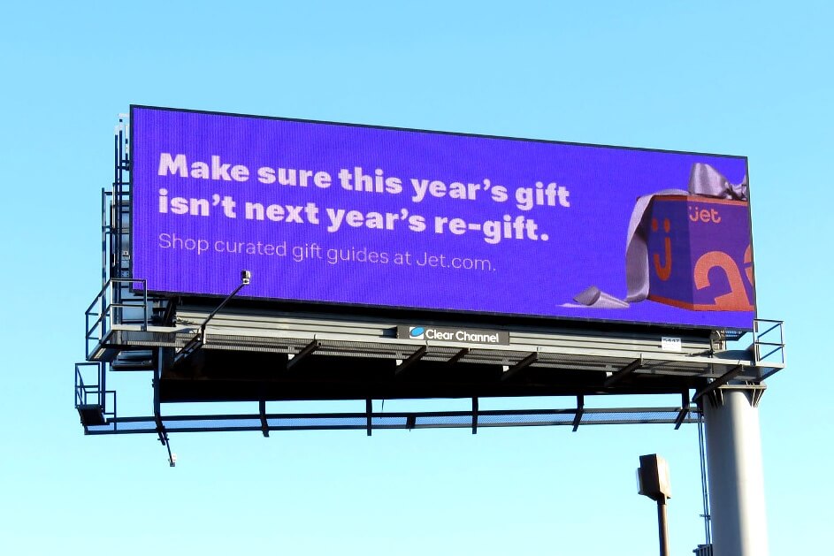 An image of a billboard for Jet.com. The billboard's background is purple with white text and has a wrapped purple box on the right-hand side with a bow.
