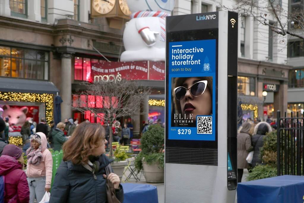An image of a busy street with a DOOH ad on a screen for Elle Eyewear.