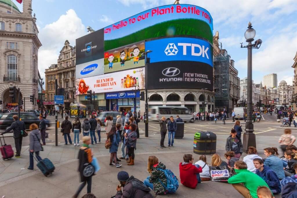 An image of a busy street corner with DOOH billboard signs and a bunch of people walking by them.