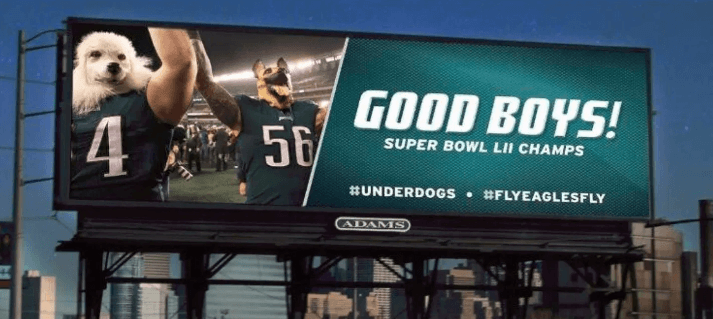An image of a billboard ad for the Super Bowl. The ad displays two football players celebrating and their heads have been replaced with dog heads.