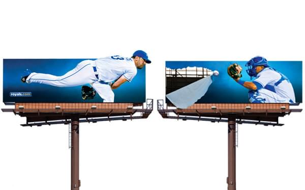 An image of two billboards side by side. It is an advertisement for royals.com and shows a baseball player on one billboard throwing a baseball to the catcher on the other billboard.