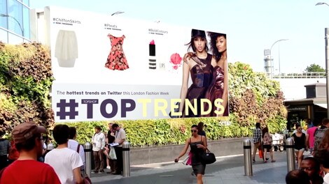 An image of a billboard promoting London Fashion Week. It has a skirt, a dress, and lipstick on it. Also has two fashion models on the far right.