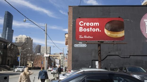 An image of a billboard advertisement for Tim Hortons. The ad says "Cream Boston" and has a picture of a Boston cream doughnut.