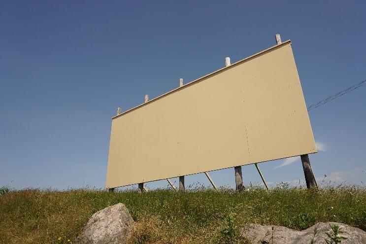 A blank billboard on top of a grassy hill.