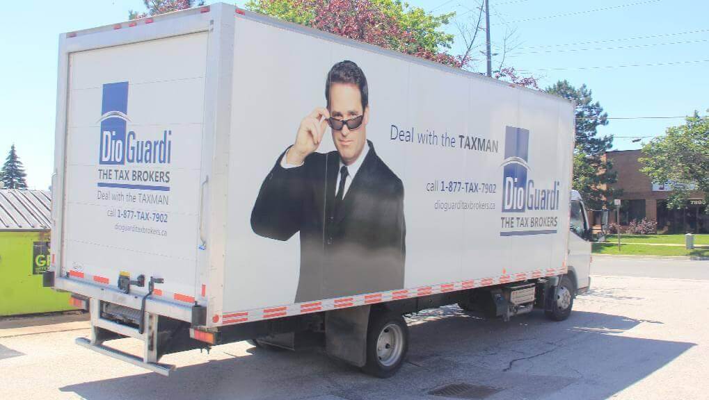 Picture of truckside mobile billboard ad for DioGuardi The Tax Brokers. Ad reads, "Deal with the TAXMAN" and provides number for people to call.