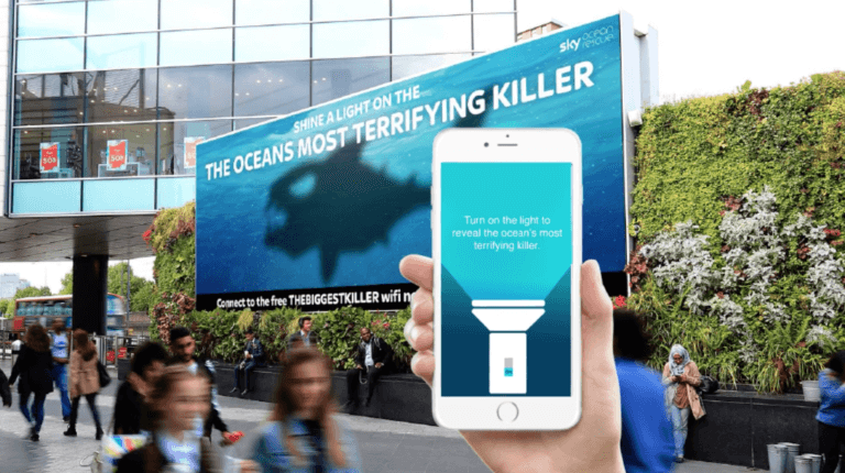A billboard showing a shark and someone holding their phone up to it with the message on the phone "Turn on the light to reveal the ocean's most terrifying killer"