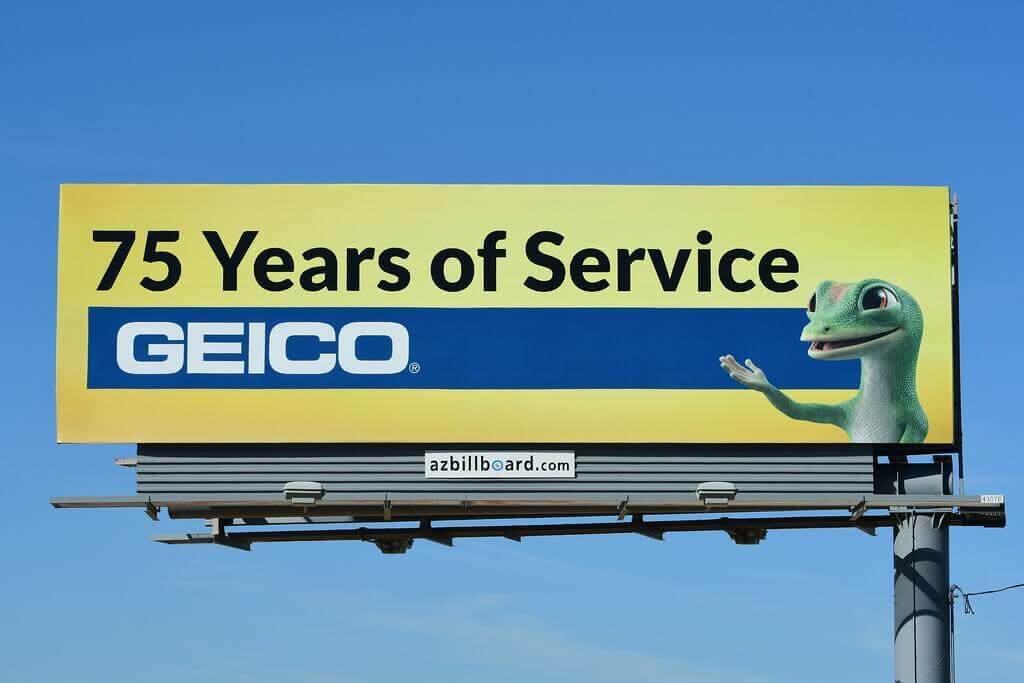 Picture of GEICO billboard featuring GEICO's Gecko mascot. Ad reads, "75 Years of Service. GEICO".