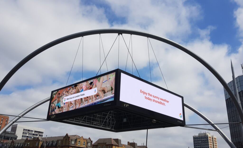 An image of a digital OOH ad for Google that has four different sides and is hoisted above a square.