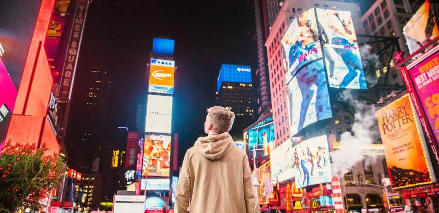 An image of a boy in the foreground looking up at all the billboards in Times Square.
