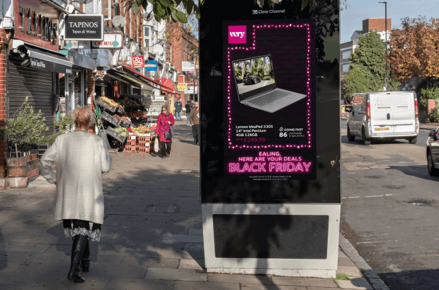An image of a woman walking along the street beside an ad for Shop Direct. The ad is in black and pink and is promoting their Black Friday sales with an image of a laptop in the centre.