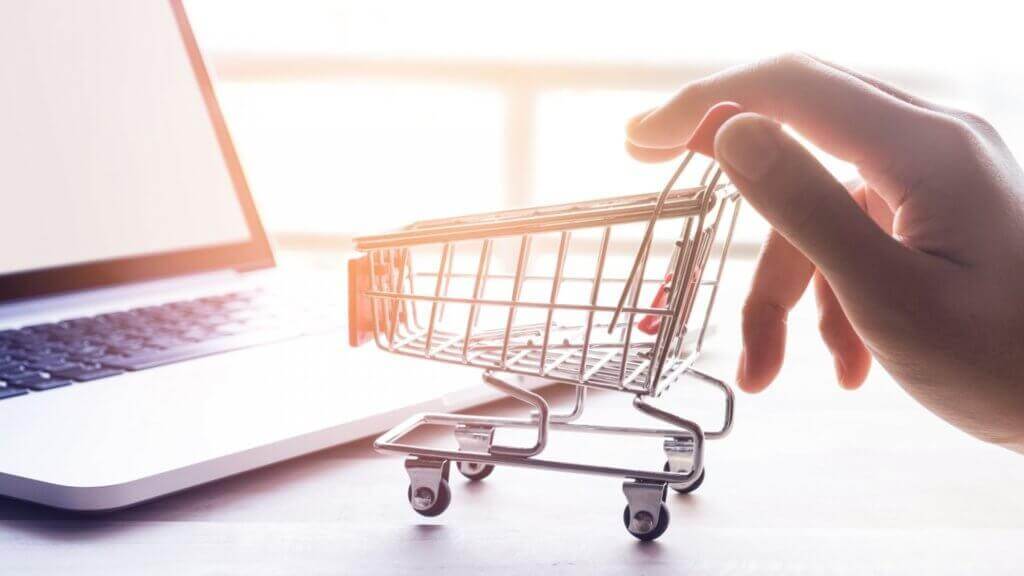 Photo of hand pushing minature shopping cart by a laptop.
