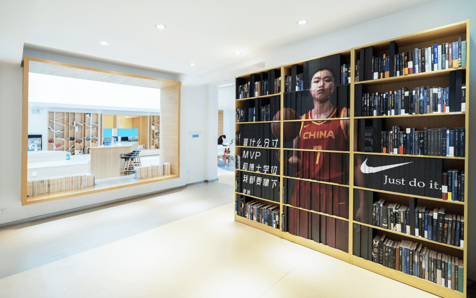 An image of a book shelf in a library where the books are colour-coordinated to demonstrate a Nike ad of Shao Ting holding a basketball. 