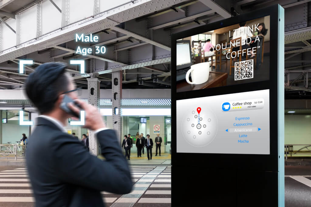 An image of a man looking at a digital OOH advertisement with a QR code. The man is being targeted by the ad.