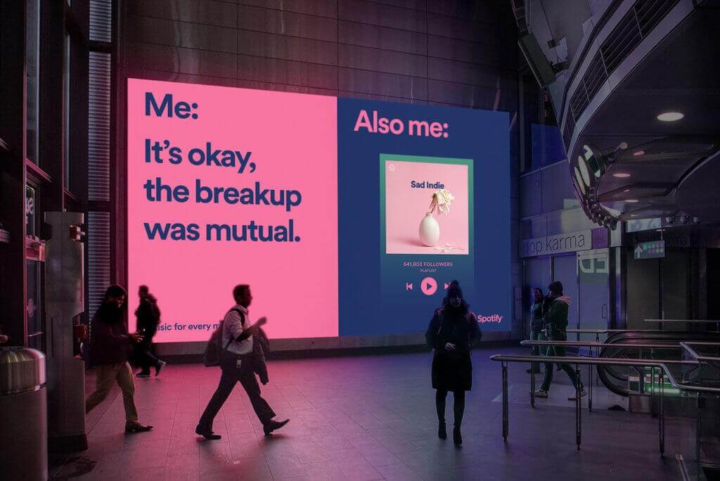 An image of a billboard for Spotify that is displayed in bright pink and dark blue. The ad shows a popular meme that says, "Me: It's okay, the breakup was mutual." and then, "Also me:" and then an image of a Sad Indie playlist.