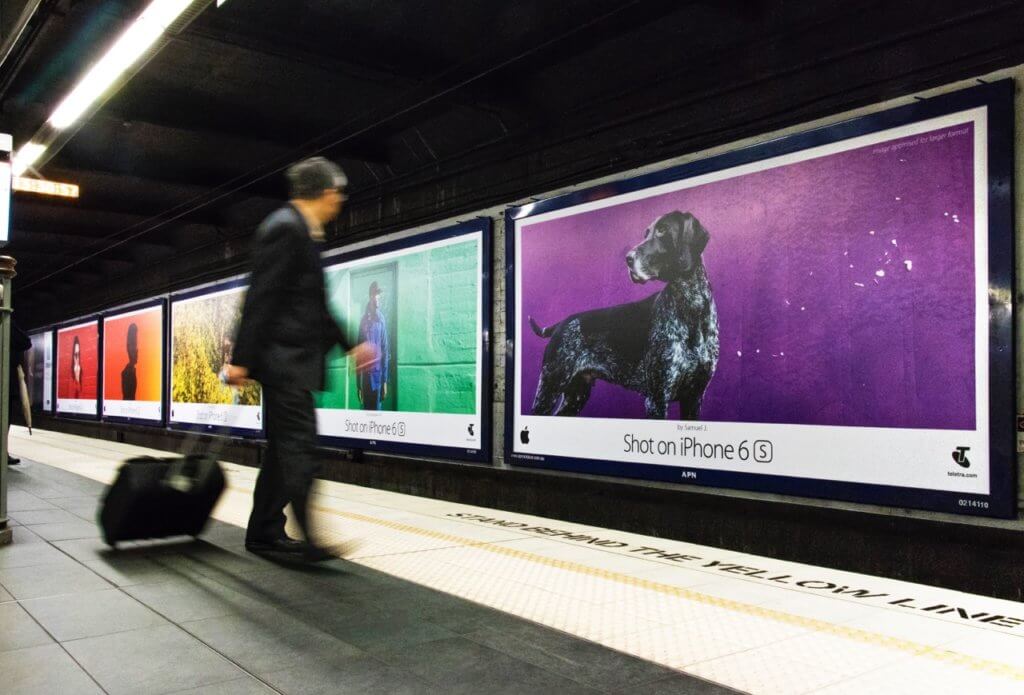 An image of a bunch of Apple ads on the side of a subway platform. All with different bold colours including red, orange, yellow, green, and purple.