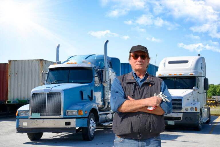 Image of a truck driver standing in front of his trucks, arms crossed.