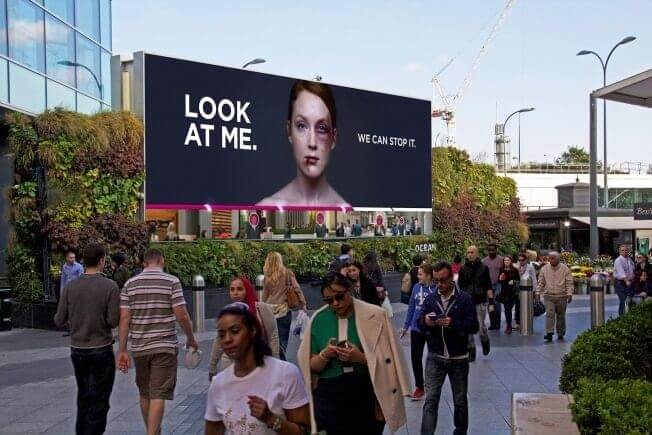 An image of an ad by Women's Ad of a battered woman with passersby in the foreground.